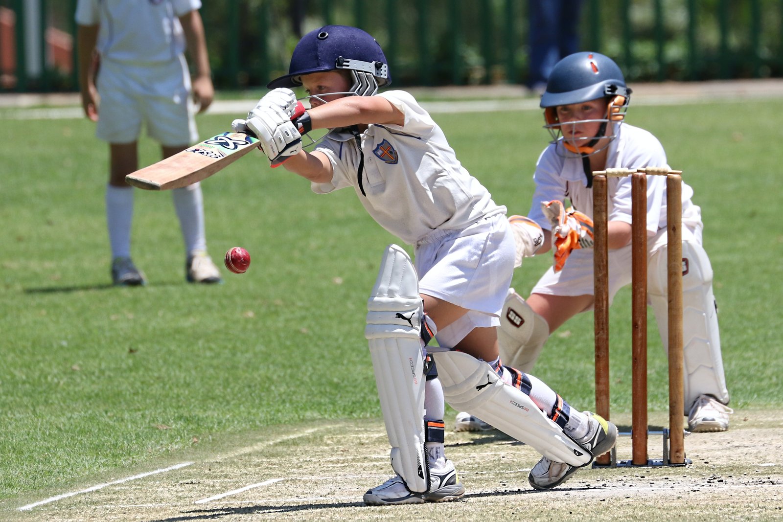A junior cricketer smashing a ball with a well-fitted bat during a match